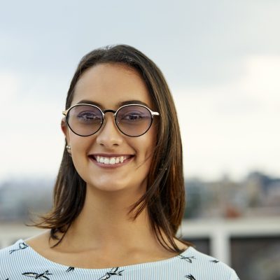 Portrait of beautiful businesswoman smiling against sky. Young female professional is wearing sunglasses. She is standing at rooftop.